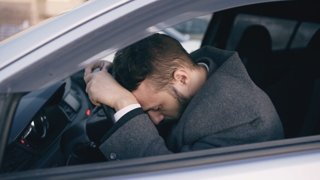 stressed man resting head on steering wheel in car