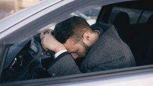 stressed man resting head on steering wheel in car